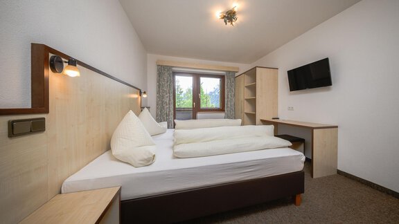 Ein modernes Schlafzimmer mit einem Doppelbett und zwei Kissen. Der Raum hat einen Schreibtisch, einen Fernseher und große Fenster mit Blick nach draußen. - Appartement Alpin - Sölden