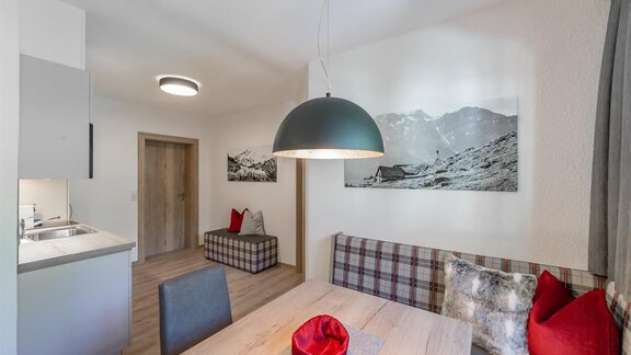 Ein modernes Esszimmer mit einem großen Holztisch und bequemen Sitzgelegenheiten. Die Wände sind mit stilvollen Fotos und einem großen Lampenleuchter dekoriert. - Appartement Cristallo - Sölden