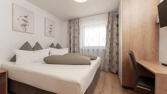 The image shows a modern bedroom with a large double bed. There are wooden and textile elements as well as a desk and a chair. - Appartement Gehörde Sölden - Sölden