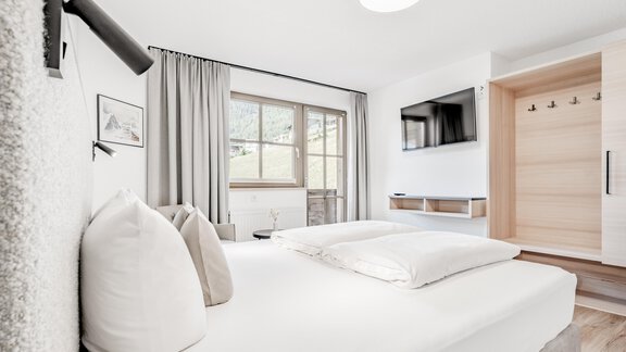 Ein helles Schlafzimmer mit einem großen Doppelbett und modernen Möbeln. Ein Fenster mit Blick auf die Natur sorgt für natürliches Licht. - Appartement Montanara - Sölden