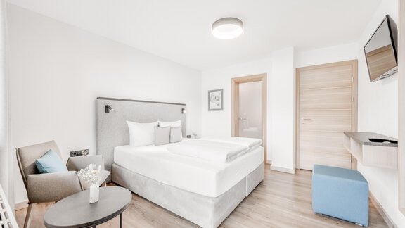 Ein modernes Schlafzimmer mit einem großen Bett und minimalistischer Einrichtung. Es gibt einen Sessel, einen Tisch und einen Fernseher an der Wand. - Appartement Montanara - Sölden