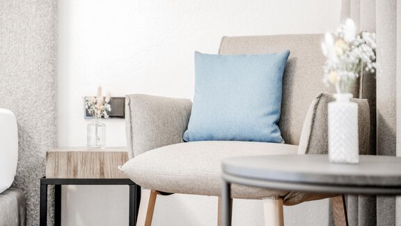 Ein moderner Stuhl mit einem blauen Kissen steht neben einem kleinen Tisch. Auf dem Tisch befindet sich eine Blumenvase mit frischen Blumen. - Appartement Montanara - Sölden