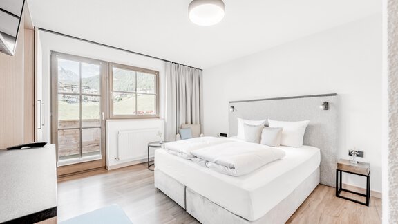 Ein modernes Schlafzimmer mit einem großen Bett und hellem Holzfußboden. Große Fenster bieten einen Blick auf die Natur draußen. - Appartement Montanara - Sölden