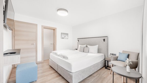 Ein modernes Schlafzimmer mit einem großen Bett und hellen Wänden. Es gibt einen kleinen Tisch und einen Stuhl sowie einen Fernseher an der Wand. - Appartement Montanara - Sölden