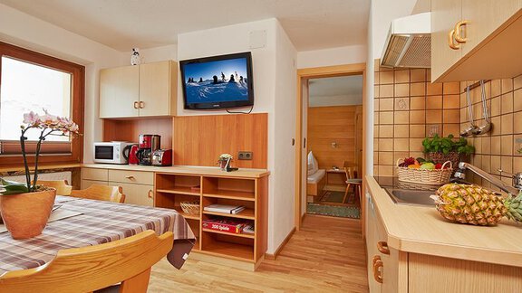Eine moderne Küche mit einem Esstisch, einem Fernseher und voll ausgestatteten Geräten. Der Holzfußboden und die warmen Farben schaffen eine gemütliche Atmosphäre. - Appartement Schwalbennest - Sölden