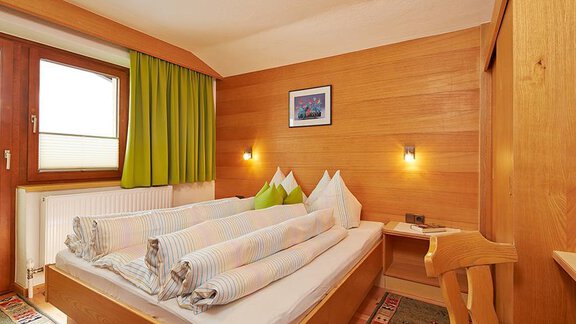 Ein gemütliches Schlafzimmer mit Holzverkleidung und einem großen Doppelbett. Die Wände sind in warmen Tönen gehalten und es gibt eine Fensterfront mit grünen Vorhängen. - Appartement Schwalbennest - Sölden