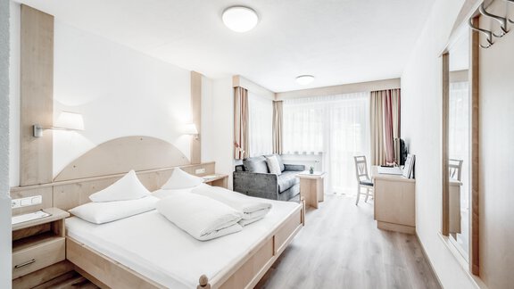 A bright hotel room with a double bed and a sofa bed. Large windows provide plenty of daylight and a welcoming atmosphere. - Appartementhaus Kathrin - Sölden