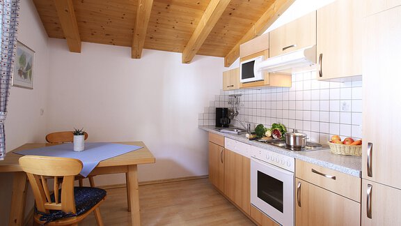 Eine moderne Küche mit Holzregalen und weißen Schränken. Ein Tisch mit Stühlen und frischen Lebensmitteln auf der Arbeitsfläche. - Appt.  Ferienglück - Sölden