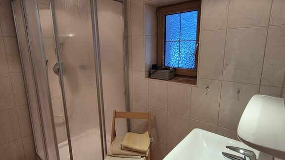 Ein modernes Badezimmer mit einer Dusche und einem Waschbecken. Es gibt einen Stuhl und ein Fenster, das Tageslicht hereinlässt. - Appt. Wildschütz - Sölden