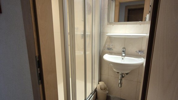 Ein kleines Badezimmer mit einer Dusche, einem Waschbecken und einem Spiegel. Der Boden ist mit Fliesen und einem Mattenbelag ausgestattet. - Appt. Wildschütz - Sölden