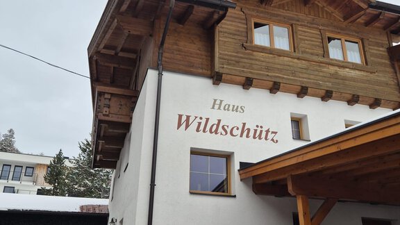 Ein gemütliches Gebäude mit einem Holzanklang und dem Namen "Haus Wildschütz" an der Fassade. Der Eingangsbereich ist überdacht und im Vordergrund liegt etwas Schnee. - Appt. Wildschütz - Sölden