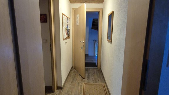 Ein heller Flur mit Holzwänden und einem Holzdeckenpanel. Am Ende des Flurs befindet sich eine offene Tür, die zu einem Raum führt. - Appt. Wildschütz - Sölden