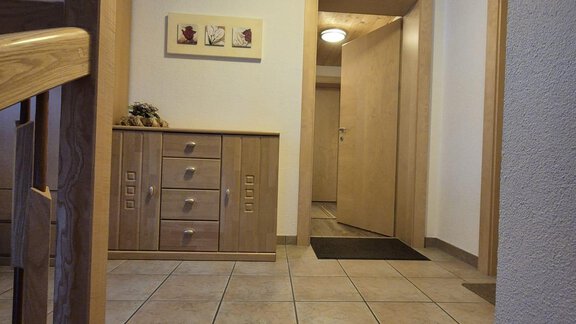 Ein heller Eingangsbereich mit Fliesenboden und Holzdetails. Es gibt eine Kommode und mehrere Türen, die zu weiteren Räumen führen. - Appt. Wildschütz - Sölden