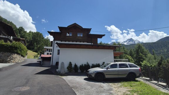 Ein modernes Haus in den Bergen mit einem asphaltieren Weg. Im Vordergrund steht ein heller SUV, umgeben von grüner Landschaft. - Appt. Wildschütz - Sölden