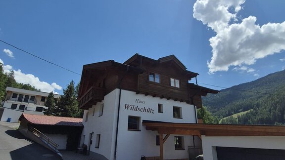 Ein typisch alpenländisches Haus mit Holzverkleidung und einem klaren blauen Himmel. Umgeben von einer malerischen Berglandschaft und grünen Wäldern. - Appt. Wildschütz - Sölden