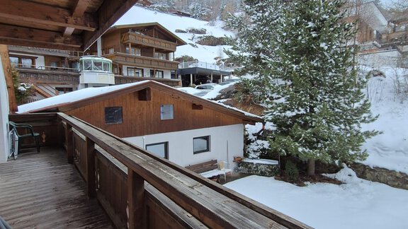 Ein Blick von einer Holztreppe auf einen verschneiten Winterort. Im Vordergrund sind Holzhäuser und ein grüner Baum sichtbar. - Appt. Wildschütz - Sölden