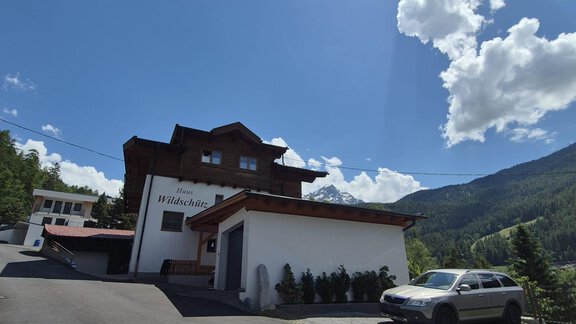 Ein modernes Gebäude in einer Berglandschaft mit klarem Himmel. Im Vordergrund steht ein Auto auf der Straße. - Appt. Wildschütz - Sölden