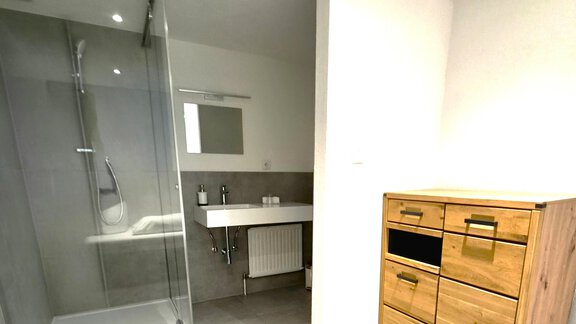 Ein modernes Badezimmer mit einer Glasdusche und einem Waschbecken. Auf der rechten Seite steht eine Holzkommode mit mehreren Schubladen. - Arno`s Hoamat - Sölden