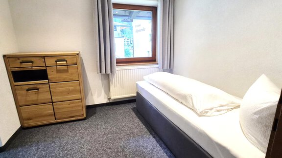 Ein einfaches, helles Zimmer mit einem Einzelbett und einem Holzschrank. Das Fenster lässt Tageslicht herein und die Wände sind neutral gehalten. - Arno`s Hoamat - Sölden