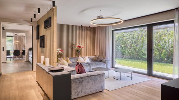 Ein modern eingerichtetes Wohnzimmer mit einem bequemen Sofa und großen Fenstern. Die Raumgestaltung ist hell und einladend, mit Blick auf einen Garten. - Chalet White Pearl by MYALPS - Sölden