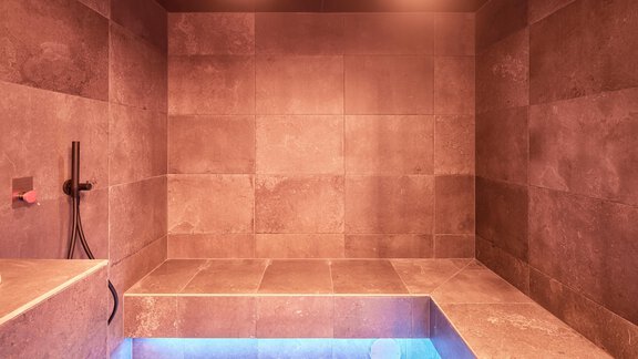 Ein moderner Wellnessbereich mit einer kleinen Sauna und einem blauen Wasserbecken. Die Wände sind aus grauen Fliesen und sanft beleuchtet. - Chalet White Pearl by MYALPS - Sölden