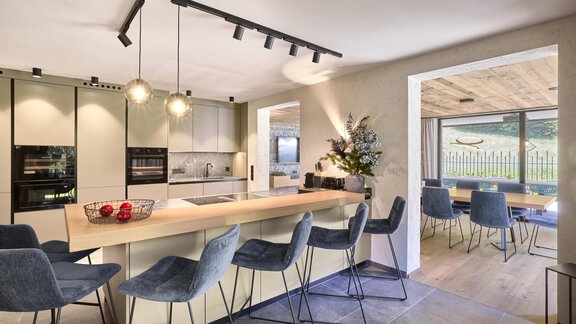 Eine moderne Küche mit einem großen Holzessenstisch und stilvollen Stühlen. Der Raum hat viel Licht und einen Blick ins Freie. - Chalet White Pearl by MYALPS - Sölden