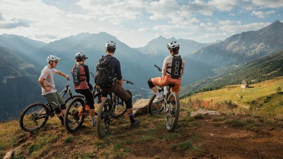 Vier Radfahrer stehen auf einem Berg und blicken in die Ferne. Im Hintergrund sind beeindruckende Berglandschaften und ein klarer Himmel zu sehen. - Chalet White Pearl by MYALPS - Sölden
