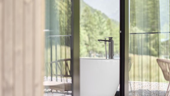 Ein modernes Bad mit freistehender Badewanne und großen Fenstern. Durch die Glastüren ist die schöne Natur im Hintergrund sichtbar. - Chalet White Pearl by MYALPS - Sölden