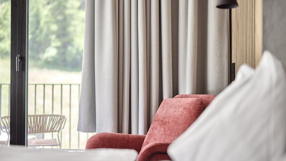 Ein modernes Zimmer mit einem roten Sessel und eleganten Vorhängen. Im Hintergrund ist ein Balkon sichtbar, der den Blick ins Freie ermöglicht. - Chalet White Pearl by MYALPS - Sölden