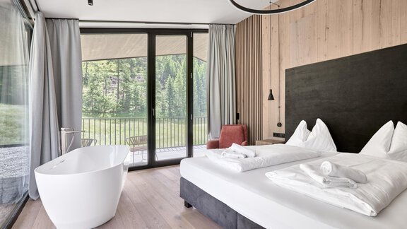 Ein modernes Schlafzimmer mit Holzverkleidung und großen Fenstern. Es gibt ein komfortables Doppelbett und eine freistehende Badewanne. - Chalet White Pearl by MYALPS - Sölden