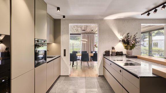 Eine moderne Küche mit eleganten, beigen Schränken und einem großen, hellen Fenster. Im Hintergrund sieht man einen Essbereich mit eleganten Stühlen und einem Tisch. - Chalet White Pearl by MYALPS - Sölden