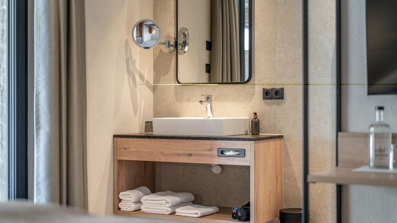 A modern bathroom with an elegant sink and a large mirror. White towels are neatly placed on a wooden shelf. - Edelweiss echt.charmant. - Sölden