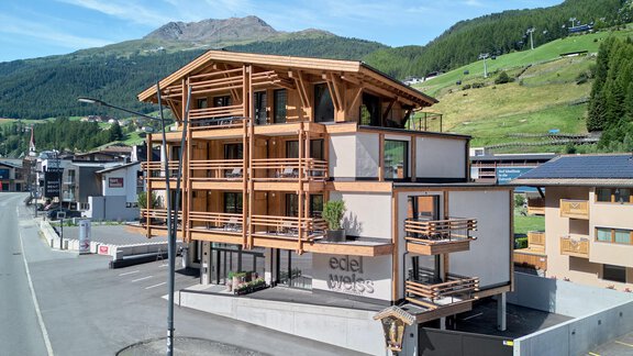 Ein modernes Gebäude aus Holz in einer bergigen Umgebung. Im Hintergrund sind grüne Hügel und ein blauer Himmel zu sehen. - Edelweiss echt.charmant. - Sölden