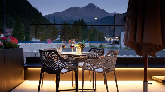 Ein gemütlicher Tisch mit Stühlen auf einer Terrasse bei Dämmerung. Im Hintergrund sind Berge zu sehen, die eine entspannte Atmosphäre schaffen. - Edelweiss echt.charmant. - Sölden