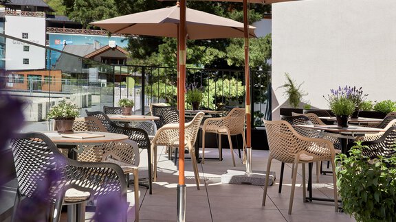 Eine Terrasse mit stilvollen Möbeln und Sonnenschirmen. Umgeben von Pflanzen bietet sie eine einladende Atmosphäre. - Edelweiss echt.charmant. - Sölden