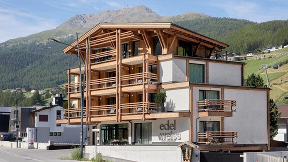 Ein modernes Gebäude mit Holzverkleidung und großen Fenstern. Im Hintergrund sind grüne Hügel und Berge zu sehen. - Edelweiss echt.charmant. - Sölden