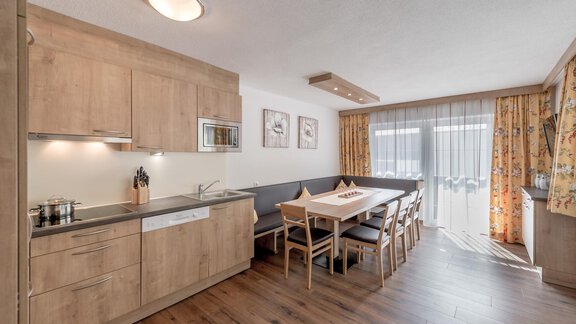 Eine moderne Küche mit Holzschränken und einem Essbereich. Das große Fenster lässt viel Licht herein und bietet einen gemütlichen Blick nach draußen. - Ferienhaus Apart Sonnzeit - Sölden