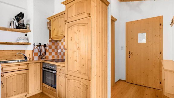 Eine gemütliche Küche aus hellem Holz mit modernen Geräten. Rechts ist eine Holztür, die zur Wohnung führt. - Garni Nadine - Sölden