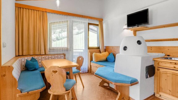 Ein gemütlicher Wohnbereich mit Holzverkleidung und blauen Polstern. Ein Tisch und Stühle bieten Platz zum Entspannen, während ein Fernseher an der Wand montiert ist. - Garni Nadine - Sölden