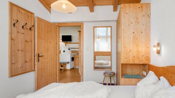Ein gemütliches Schlafzimmer mit Holzmöbeln und einem Blick auf ein angrenzendes Zimmer. Die Wände sind hell, und das Bett ist mit weißen Decken ausgestattet. - Garni Nadine - Sölden