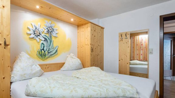Ein gemütliches Schlafzimmer mit einem großen Bett und Holzverkleidung. An der Wand hängt ein Gemälde von Blumen, das den Raum belebt. - Garni Nadine - Sölden