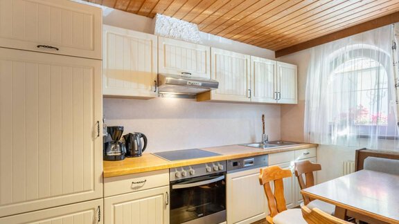 Eine moderne Küche mit hellen Schränken und Holzdecken. Der Tisch ist mit Stühlen versehen und es gibt einen Herd und eine Kaffeemaschine. - Garni Nadine - Sölden