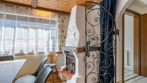 Ein gemütlicher Raum mit einem Kamin und einem Holztisch. Die Fenster lassen viel Licht herein und die Dekoration ist einladend. - Garni Nadine - Sölden