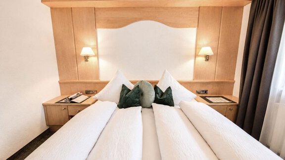 A cozy bedroom with two beds and soft, white bedspreads. The walls are made of light wood, and there is soft lighting as well as decorative cushions. - Garni Rustica - Sölden