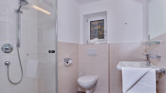 Ein modernes Badezimmer mit einer Dusche, einem Waschbecken und einer Toilette. Die Wände sind hell und das Design ist schlicht und sauber. - Gästehaus Bergkristall - Sölden