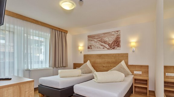 Ein gemütliches Hotelzimmer mit zwei Einzelbetten und modernem Holzinterieur. Große Fenster lassen viel Licht herein und sorgen für eine freundliche Atmosphäre. - Gästehaus Bergkristall - Sölden