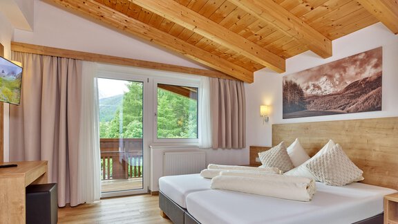 A modern bedroom with a wooden ceiling and large windows that let in a lot of light. The decor is simple and cozy, with two beds and a television. - Gästehaus Bergkristall - Sölden