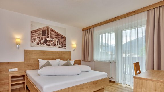 Ein modernes Schlafzimmer mit einem großen Bett aus Holz und einem freundlichen Ambiente. Große Fenster lassen viel Licht herein und bieten einen Blick auf die Natur. - Gästehaus Bergkristall - Sölden