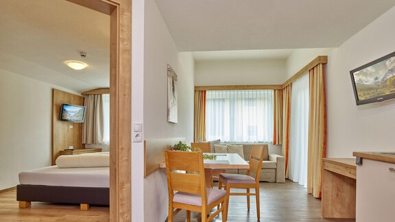 Ein helles und modernes Zimmer mit einem gemütlichen Essbereich und großen Fenstern. Der Raum ist mit Holzmobiliar und einem Fernseher ausgestattet. - Gästehaus Bergkristall - Sölden
