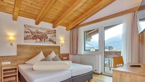 Ein modernes Schlafzimmer mit einem Holzdecke und großen Fenstern. Es gibt ein bequemes Bett und einen Blick auf die Berge. - Gästehaus Bergkristall - Sölden
